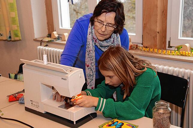 Konzentriert fädelt Maria (9) den Faden in die Maschine ein, Ruth Binkert schaut der jungen Näherin interessiert zu.