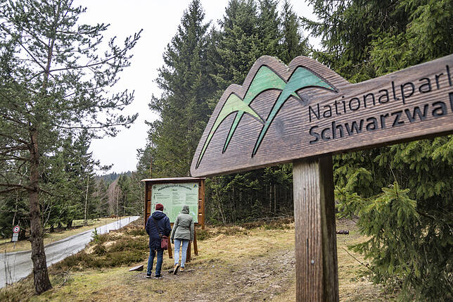 Besucher lesen eine Tafel am Eingang zum Nationalpark Nordschwarzwald.