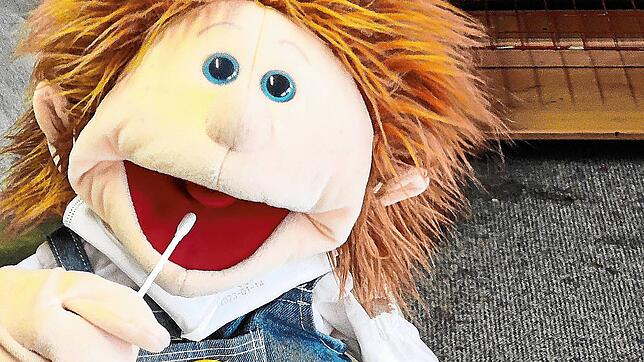 Puppe Theo macht vor, wie der Lollitest funktioniert. So können Kinder spielerisch vorbereitet werden.