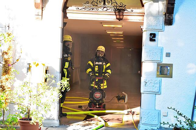Die Feuerwehrleute stehen mit Atemschutz im Eingangsbereich des Hauses.
