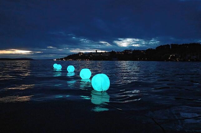Diese illuminierten Ballons hinter dem Begleitboot helfen auf ihrem Weg von Bodman nach Bregenz in der Nacht zur Orientierung geholfen. ...