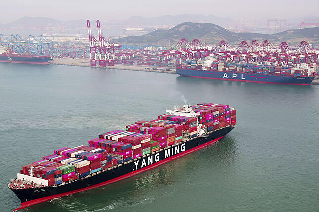 Ein Containerschiff fährt vor einem chinesischem Containerterminal. Der Handelskonflikt zwischen den USA und China wirkt sich negativ ...