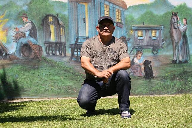 Alexander Flügler in seinem Garten. An die Wand hat er ein Bild einer typischen Szene aus dem jenischen Familienleben malen lassen: Ein ...