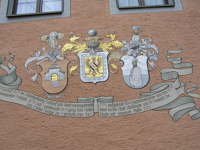 Das Bild am Amtshaus zeigt drei Wappen, der Text darunter gibt Einblick in die geschichtliche Entwicklung des Gebäudes.