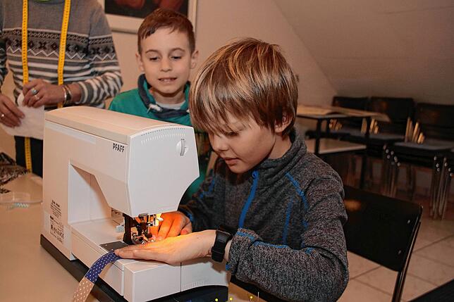 Mit Bedacht benutzt Linus (9) die Nähschine, die Naht soll schließlich gerade werden. Samuel (8) beobachtet ihn und wartet geduldig, bis ...