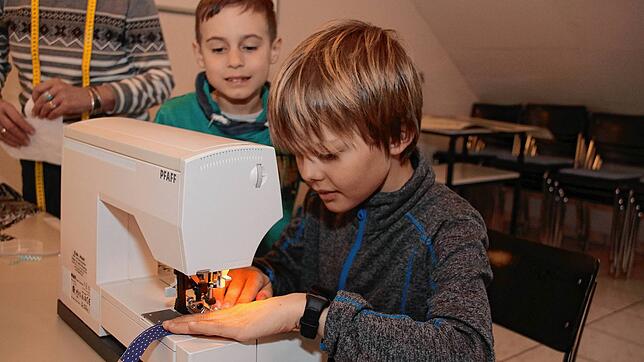 Mit Bedacht benutzt Linus (9) die Nähschine, die Naht soll schließlich gerade werden. Samuel (8) beobachtet ihn und wartet geduldig, bis ...