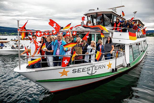 Passagiere und Besatzung des Passagierschiffes „Seestern“ schwenken während einer Sternfahrt auf dem Bodensee deutsche und ...