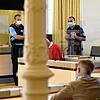 Der angeklagte Erpresser (im roten Pullover) sitzt zwischen Justizbeamten auf der Anklagebank und liest ein Dokument. Bild: dpa