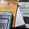 Symbolfoto: Ein Impfpass und ein Smartphone, auf dem die App CovPass läuft, liegen auf einem Impfzertifikat.