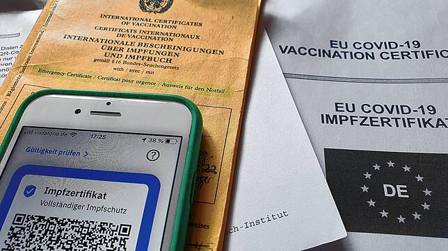 Symbolfoto: Ein Impfpass und ein Smartphone, auf dem die App CovPass läuft, liegen auf einem Impfzertifikat.