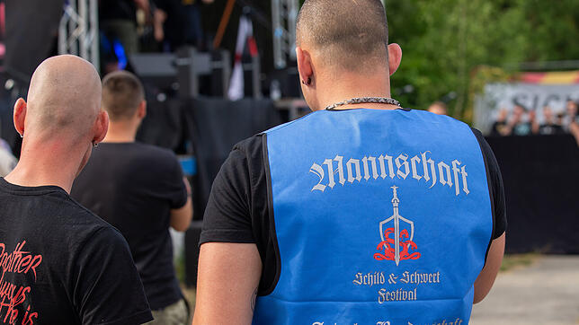 Männer stehen in Ostritz auf dem Gelände des Hotels Neißeblick, wo das Rechtsrockfestival Schild und Schwert stattfindet, vor einer ...
