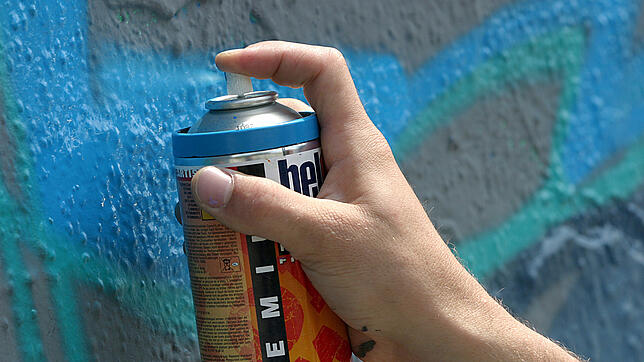 (Symbolbild) Ein Sprayer besprüht eine Wand mit Graffiti.