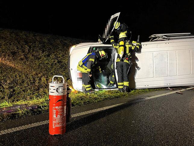 Einsatzkräfte der Feuerwehr bereiten am umgekippten Wagen das Abklemmen der Autobatterie vor, damit kein Brand entstehen kann.