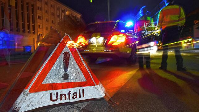 Symbolfoto: Ein Polizeifahrzeug steht mit Blaulicht auf der Straße. Daneben steht ein Warndreieck mit dem Schriftzug &ldquo;Unfall&bdquo;.