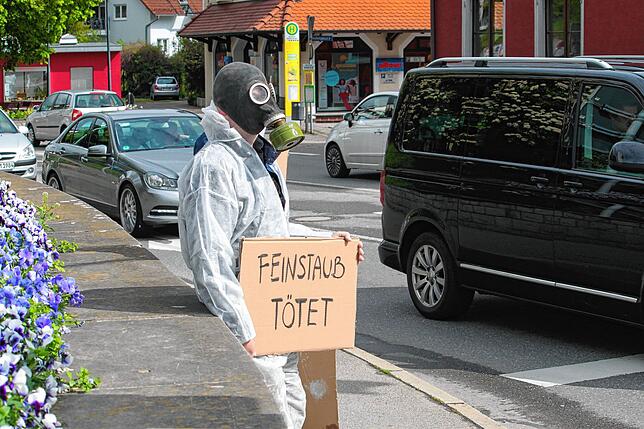 Einer der Aktivisten steht an der Bundesstraße 33, trägt eine Gasmaske und hält eine Papptafel &bdquo;Feinstaub tötet&ldquo;.