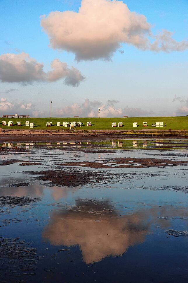 Strand bei Ebbe, Strandkörbe und die Wolken spiegeln sich im Wasser. Foto: Ulrich Wichert