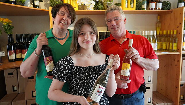 Sylvia, Sophia und Mathias Dilger mit und vor den oft prämierten Weinen.