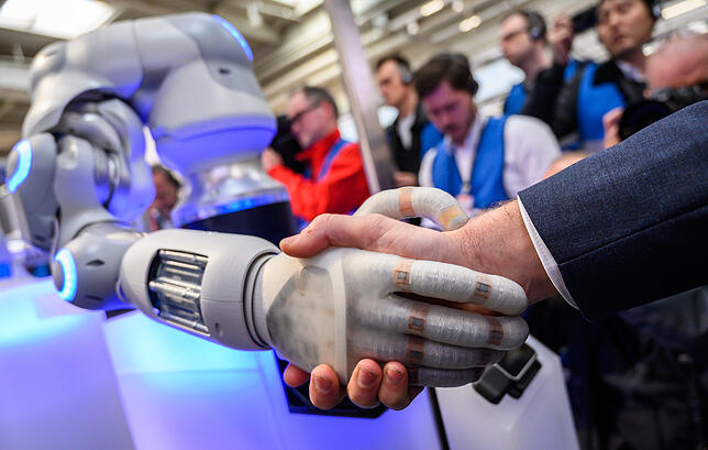 Am Stand der Unternehmensgruppe Festo begrüßt ein Roboter einen Messe-Besucher mit Handschlag.