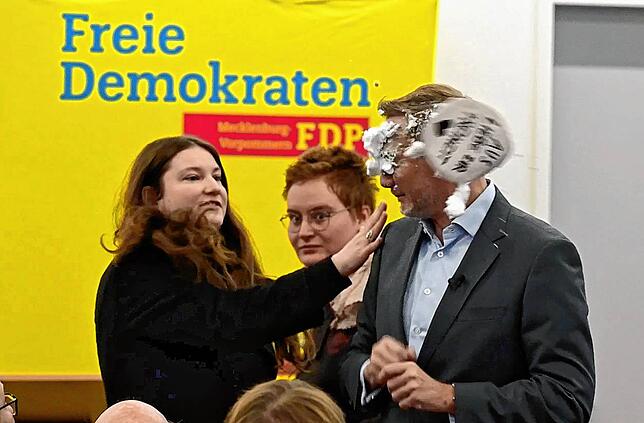 Eine junge Frau wirft Christian Lindner eine Schaumtorte ins Gesicht.