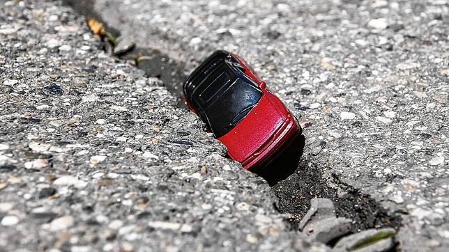 Ein Modellauto steckt in einer brüchigen Teerschicht fest. Hier ein Symbolbild für Straßenschäden.