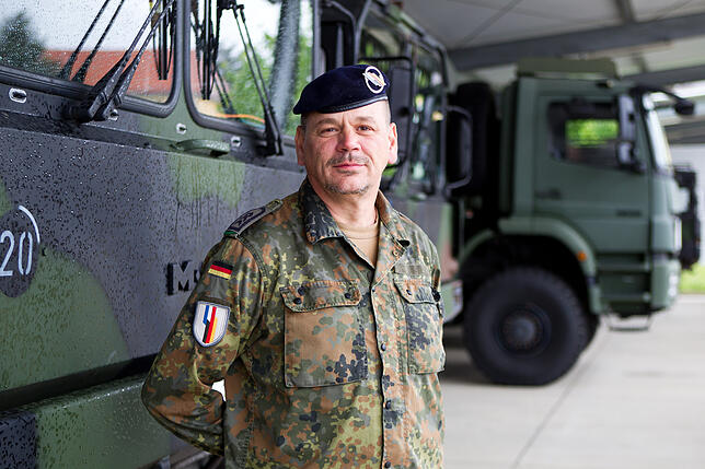Lars F., Stabsfeldwebel bei der deutsch-französischen Brigrade in Müllheim, steht vor Militärfahrzeugen der Brigade.