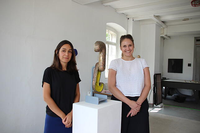 Irene Pérez Hernández (links) und Viktoria Tiedeke vor der Skulptur einer bronzenen Uhr, deren Zeiger stets in die Vergangenheit weisen.