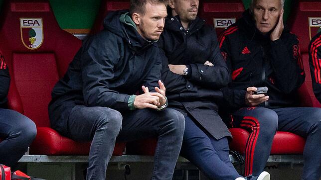 Bayerns Trainer Julian Nagelsmann (l) sitzt während der Partie beim FC Augsburg auf der Trainerbank.