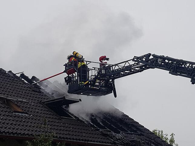 Von der Drehleiter aus bekämpfen Feuerwehrleute das Feuer durchs offene Dach.