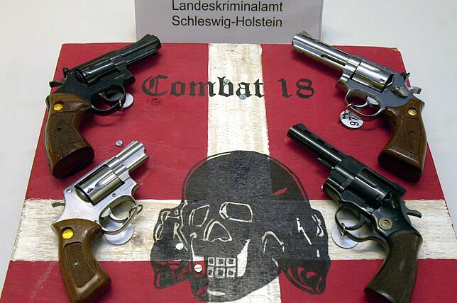 Archivbild: Sichergestellte Waffen und ein Schild der kriminellen Neonazi-Gruppe “Combat 18„ liegen im ...
