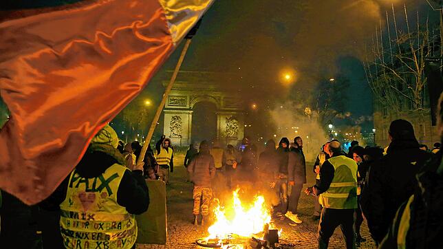 Demonstranten mit gelben Westen stehen neben einem brennenden Fahrrad auf der Champs-Elysees. Mit deutlich weniger Teilnehmern als noch ...