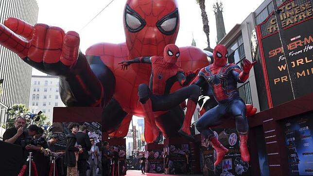 Zwei Darsteller in Spider-Man-Kostümen springen vor einem aufblasbaren Spinnenmann über den roten Teppich bei der Weltpremiere eines ...