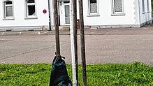 Vor dem Lauchringer Bahnhof hängt ein Bewässerungssack an einem Stützpfahl neben einem noch jungen Baum.