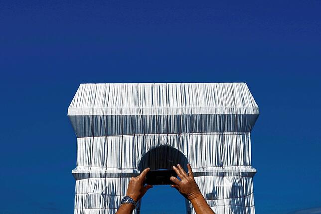 Eine Person macht ein Foto mit seinem Telefon vom Triumphbogen, der während eines Kunstprojektes in Stoffe gehüllt ist. Der Arc de ...