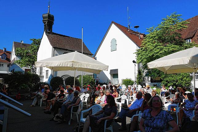 Das Publikum vor Beginn des Konzerts. Sonnenschirme und die schattenspendenden Kastanien ermöglichen ein Konzert im Freien.
