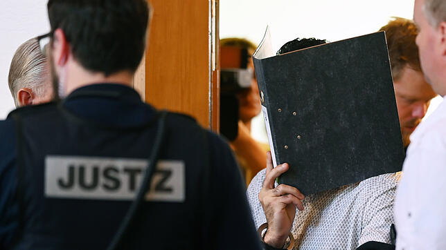 Einer von elf Angeklagten wird vor dem Prozessbeginn von einem Justizbeamten in einen Gerichtssaal im Landgericht gebracht.