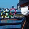 Japan, Tokio: Ein Mann, der eine schützende Gesichtsmaske trägt, geht nahe der Olympischen Ringe in der Bucht von Tokio, nachdem diese ...