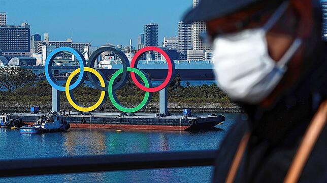 Japan, Tokio: Ein Mann, der eine schützende Gesichtsmaske trägt, geht nahe der Olympischen Ringe in der Bucht von Tokio, nachdem diese ...