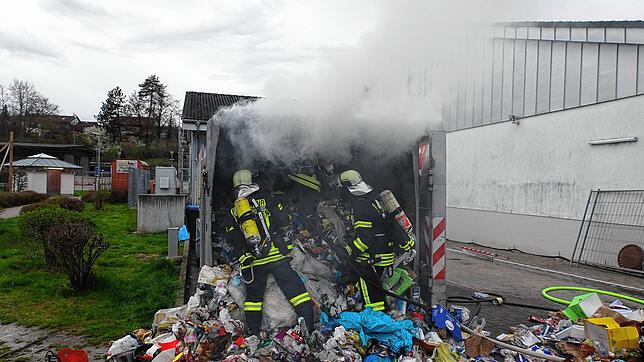 Feuerwehrleute löschen den brennenden Müll in einem Container.