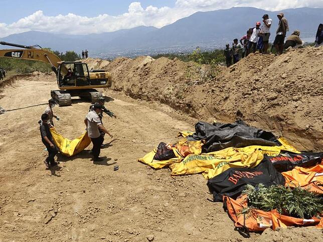 Massengrab in Palu Massenbestattung: Die indonesische Polizei bringt die Leiche eines Tsunami-Opfers zu weiteren Leichensäcken.