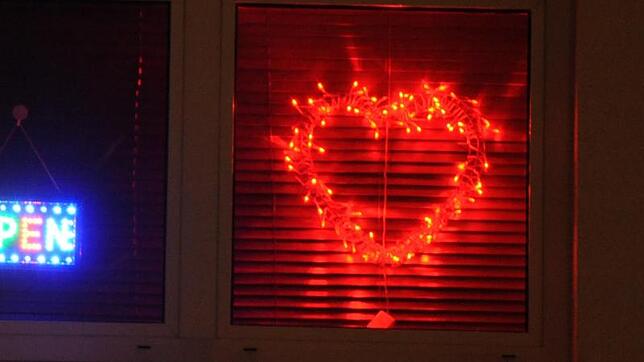 Eine Leuchtreklame in Form eines roten Herzens an einem Fenster.