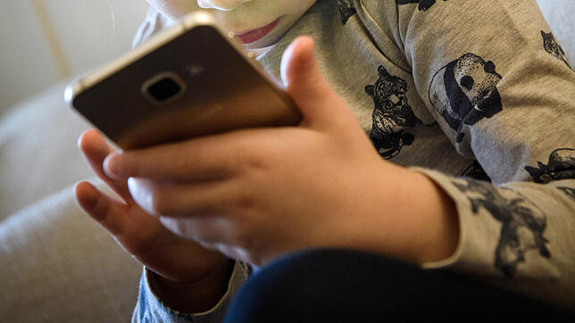 Ein kleines Mädchen schaut auf das Display eines Smartphones. Diese alltägliche Szene verdeutlicht, wovor Manfred Spitzer warnt: Kinder ...