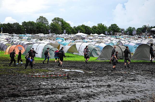 Metal-Fans sind auf dem schlammigen Festivalgelände unterwegs.