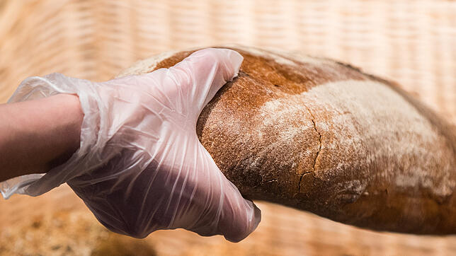 Eine Bäckereifachverkäuferin greift in einer Bäckerei mit einem Handschuh nach einem Brot.