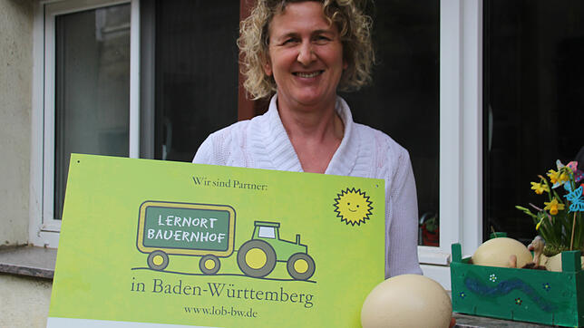 Ingrid Frick zeigt eines der Eier, die ihre Strauße gelegt haben, und das Schild, das sie als teilnehmenden Betrieb des Projekts Lernort ...