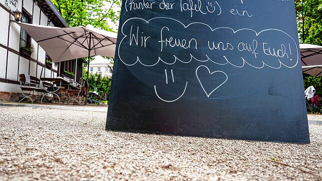 Eine Tafel mit den Worten &bdquo;Wir freuen uns auf Euch&ldquo; steht auf einer Tafel am Eingang einer Gartenterrasse. Ab 30. Mai dürfen ...