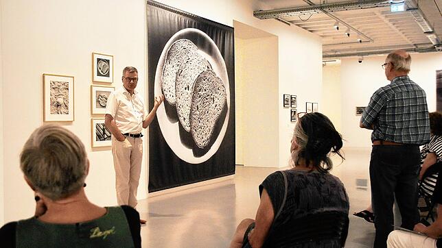 Museumsleiter Christoph Bauer hat drei Brotscheiben auf einem Bild der Ausstellung &bdquo;Schaut her! Toni Schneiders&ldquo; im Singener ...