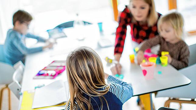 Eine Mutter, selbst von Beruf Lehrerin, sitzt mit ihren drei Kindern im Wohnzimmer und hilft ihnen bei ihren Aufgaben für die Schule. ...
