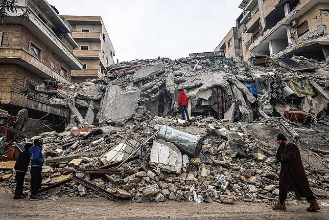 Menschen betrachten die Trümmer eines zerstörten Wohnhauses im syrischen Idlib.