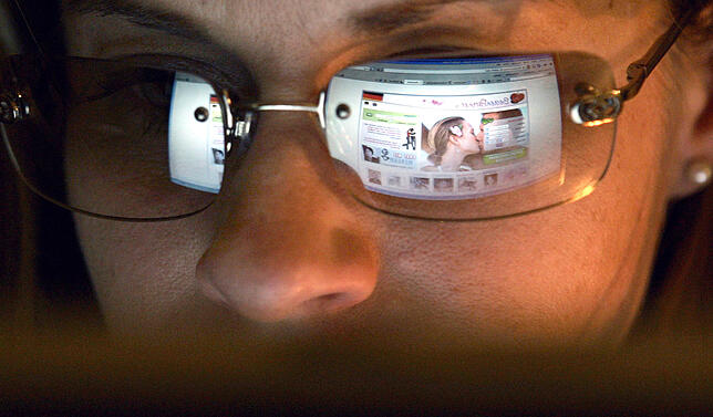 In der Brille einer jungen Frau spiegelt eine Internetseite zur Partnersuche.