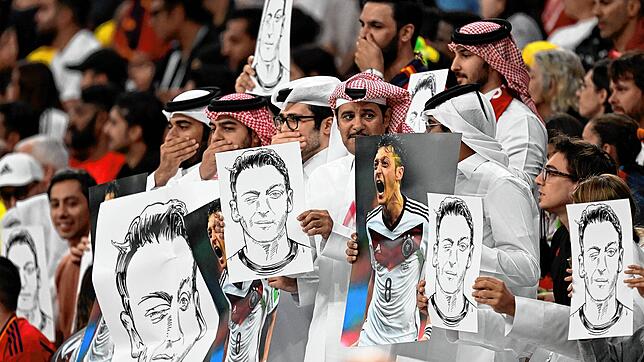 Zuschauer halten im Al-Bait Stadion in Katar Bilder von Deutschlands ehemaligem Nationalspieler Mesut Özil in die Höhe und halten sich ...